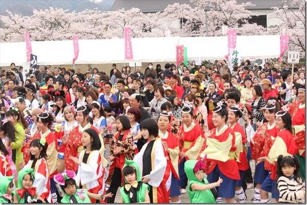 桜が咲いているさくらまつりにて様々な衣装を着た人々が踊りを踊っている写真